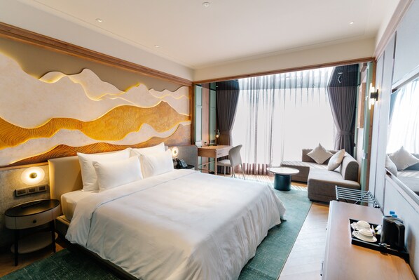 Ein Hotelzimmer mit einem großen Bett, einem Schreibtisch, einem Sessel, einer Couch und Blick ins Freie.