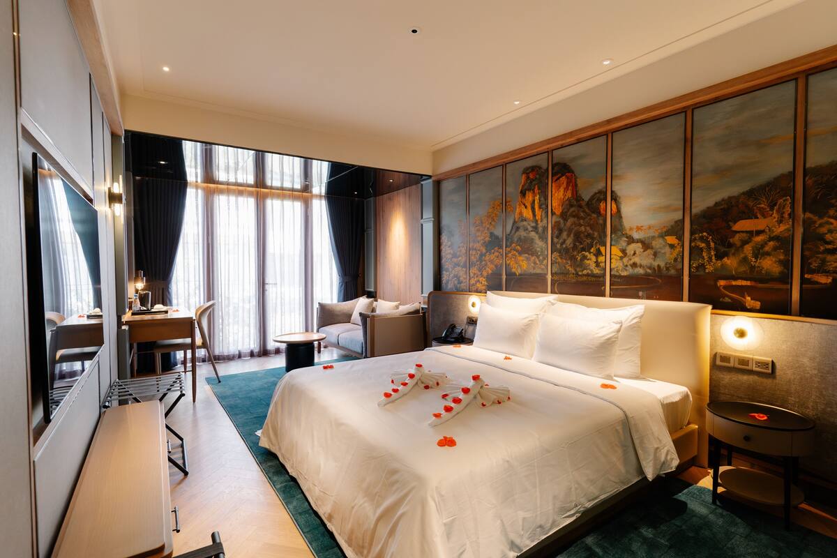 A hotel room with a large bed, a desk, a chair, and a painting on the wall.