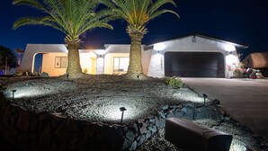 Ein modernes Haus mit zwei Palmen, einer Garage und einer gut beleuchteten Auffahrt bei Nacht.