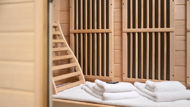 A wooden spa bath with a wooden ladder and a stack of white towels.
