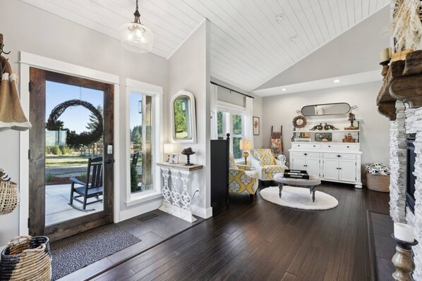 A spacious living room with a large window, a fireplace, and a dining area with a white cabinet and a mirror.