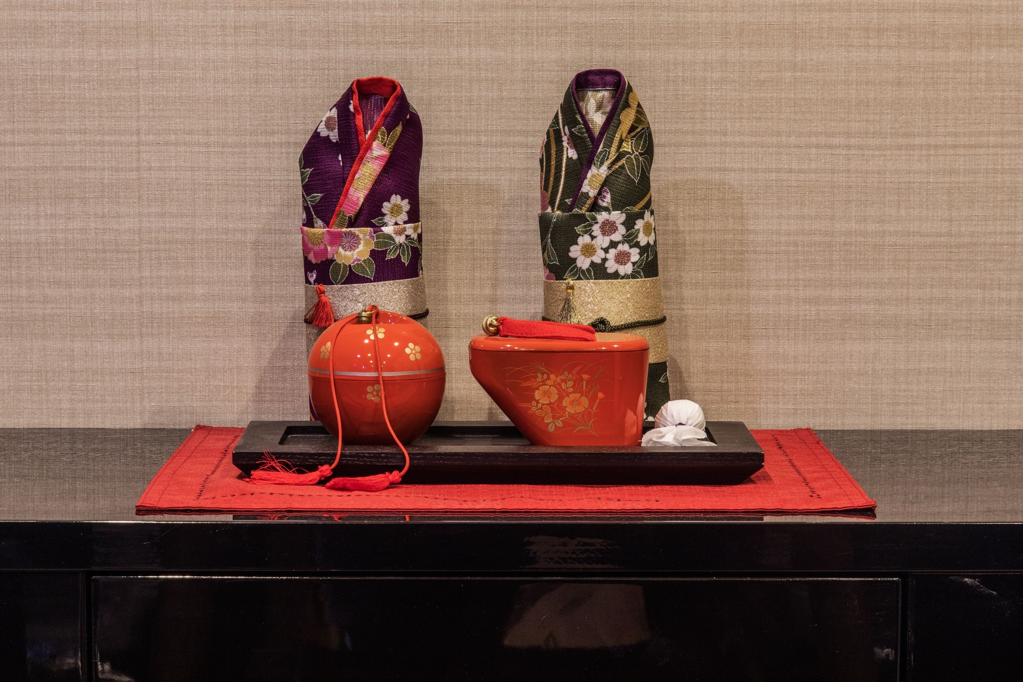 A display of traditional Japanese items including a kimono, a red lacquered container, and a white object on a black tray against a beige background.
