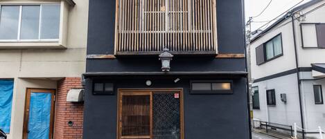 Un edificio de dos pisos con fachada oscura, una puerta de madera y un portón metálico.