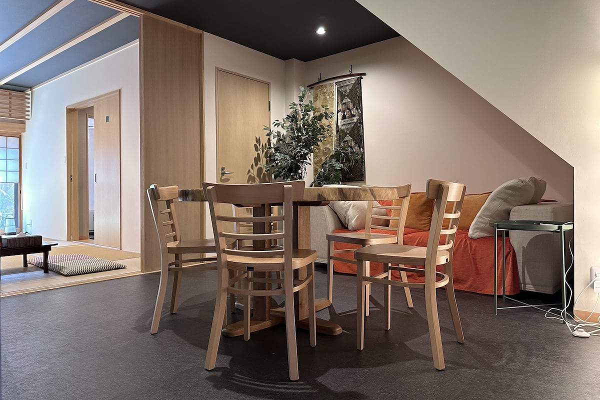 A modern dining area with wooden furniture, a large plant, and a view of a traditional building through a window.