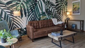 A cozy living room with a brown leather sofa, a wooden coffee table, and a large tropical leaf-patterned wall. - Casa Ceylon by Lake Seneca (Dundee)