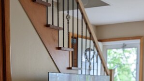 A modern living room with a wooden entertainment center, a flat-screen TV, and a staircase. - Casa Ceylon by Lake Seneca (Dundee)