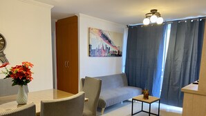 Een woonkamer met een bank, een eettafel met stoelen, een bijzettafeltje met decoratie, en een schilderij aan de muur.