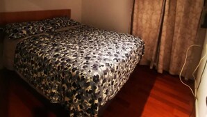 Een slaapkamer met een bed, houten vloer, gordijnen en een lamp.