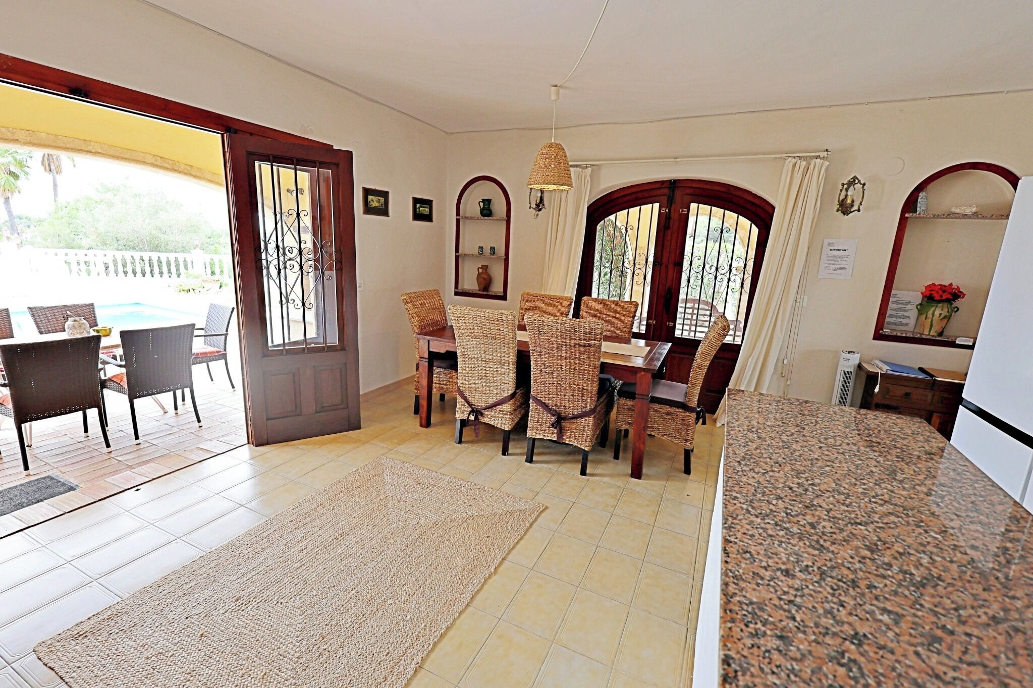 Un comedor con sillas de mimbre, encimera de granito y vista a través de una puerta de cristal.