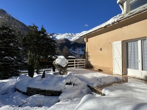 A snow-covered outdoor area with a stone wall, a wooden fence, and a building with a beige exterior and a white door.