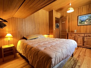 A wooden-paneled bedroom with a large bed, two bedside lamps, a nightstand, and a dresser with a mirror.