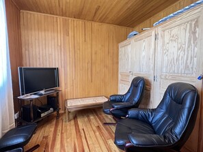 A room with wooden walls, a television on a stand, two leather chairs, and a bench.