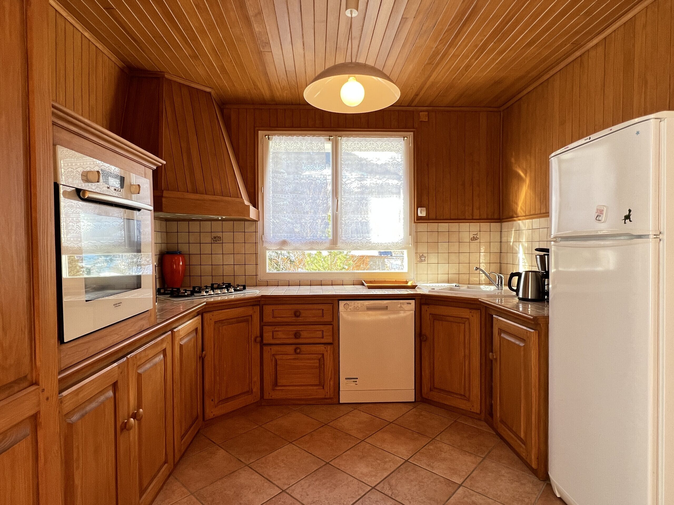 A kitchen with wooden cabinets, a built-in oven, a dishwasher, and a refrigerator.