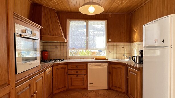 A kitchen with wooden cabinets, a built-in oven, a dishwasher, and a refrigerator. - Chalet 5 chambres / 10p (Cauterets)