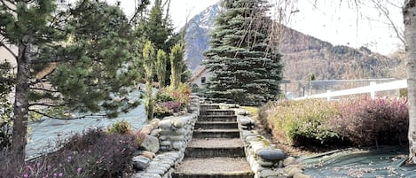 Un escalier en pierre menant à un point de vue sur la montagne, entouré d’arbres et d’arbustes.