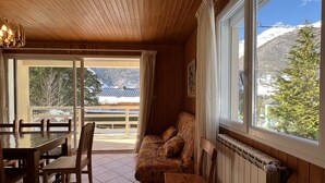 A cozy room with a wooden ceiling, a dining table with chairs, a sofa with patterned cushions, and a view of snow-covered mountains through large windows. - Chalet 5 chambres / 10p (Cauterets)