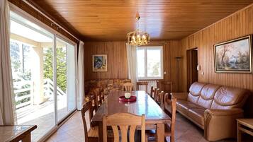 A dining area with a wooden table and chairs, a sofa, and a chandelier.