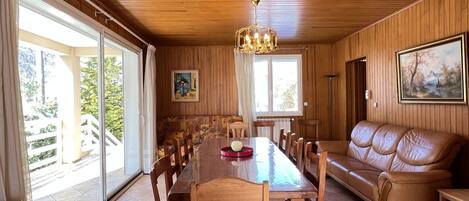 A dining area with a wooden table and chairs, a sofa, and a chandelier.