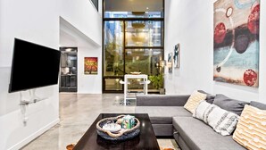 A modern living room with a flat-screen TV, a gray sofa with patterned cushions, a coffee table with a woven basket, and a large abstract painting. - Elegant design meets optimal location amid the natural beauty of Downtown Redmond. (Redmond)
