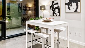 A modern dining area with a white table and bar stools, large windows with a view of a building, and two abstract paintings on the wall. - Elegant design meets optimal location amid the natural beauty of Downtown Redmond. (Redmond)