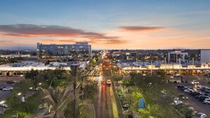 A cityscape at dusk with a prominent hotel featuring a modern design, a central road, and surrounding commercial buildings. - SCH04 · Mokulua Studio suite. hōʻoluʻolu (Chandler)