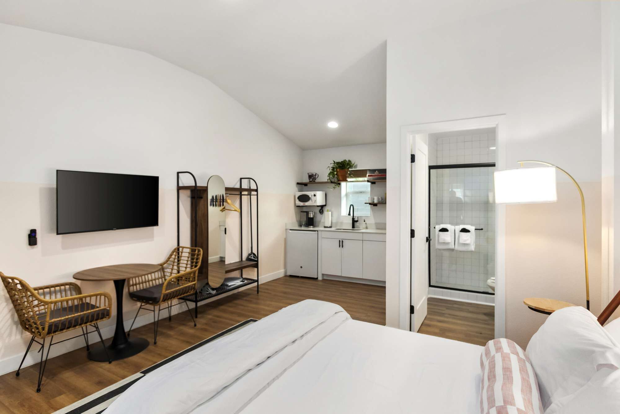 Una moderna camera d'hotel con un letto, un'area pranzo con sedie, una cucina con forno a microonde e un bagno con doccia.