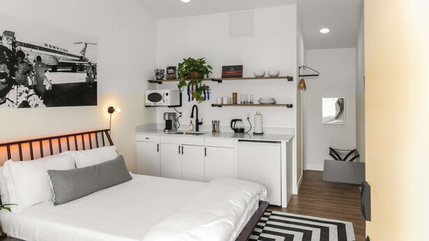 Een moderne, compacte hotelkamer met een bed, kitchenette en een klein zite hoekje.