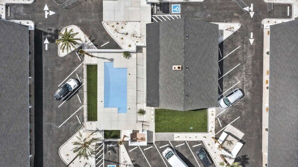 Vue aérienne d’un parking avec de nombreuses places, une piscine bleue et des palmiers.