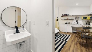 Een compacte keuken met witte kastjes, een ronde spiegel en een zwart-wit strepen tapijt.