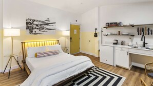 Een moderne hotelkamer met een bed, bedlamp, een klein bureau en een kitchenette.
