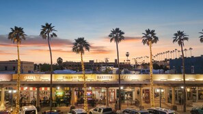 A street view at dusk with a row of shops including a barbershop, cafe, and a place named 'Mingle & Graze'.