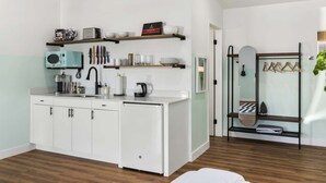 A modern kitchen with white cabinets, a microwave, and a coffee machine. There are shelves above the counter holding various kitchen items. - SCH24 - Pohakulua Studio suite.nui (Chandler)