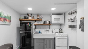 A compact kitchen with a black refrigerator, white sink, and stove, wooden shelves above the sink, and a microwave above the stove. - CC01 - Columbia City Urban Studio (Seattle)