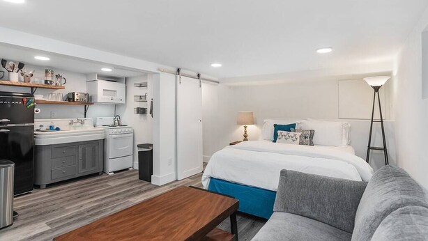 A modern hotel room with a kitchenette, a bed with a blue accent, a grey sofa, and a wooden coffee table. - CC01 - Columbia City Urban Studio (Seattle)