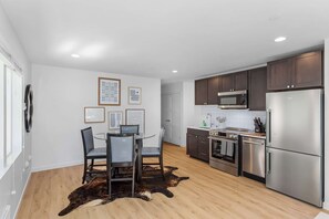 A modern kitchen with stainless steel appliances, dark wooden cabinets, and a dining area with a glass table and chairs. - CH09 - The Sweetest Hill - 81 Walkscore! (Seattle)