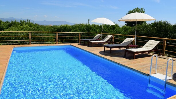 Una piscina rectangular con cubierta de madera y sillas de descanso con sombrillas.