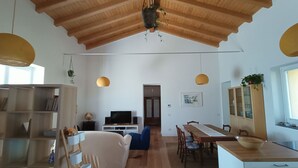 Amplia sala de estar con techo de madera alto, televisor y mesa de comedor con sillas.