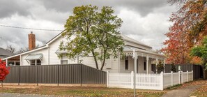 A white house with a porch, a brick chimney, and a metal fence. - Central Bendigo Cottage Charm (Bendigo)