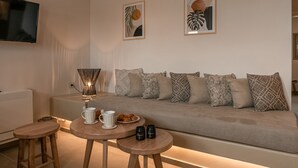 A modern living room with a sofa, two side tables, a flat-screen TV, and artwork on the wall. - Living Moments (Santorini)