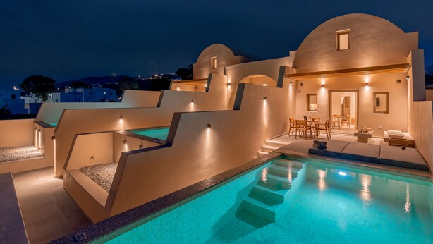 A modern pool area with a clear blue pool, sun loungers, and a seating area with tables and chairs. - Living Moments (Santorini)