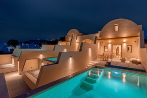 A modern pool area with a clear blue pool, sun loungers, and a seating area with tables and chairs. - Living Moments (Santorini)