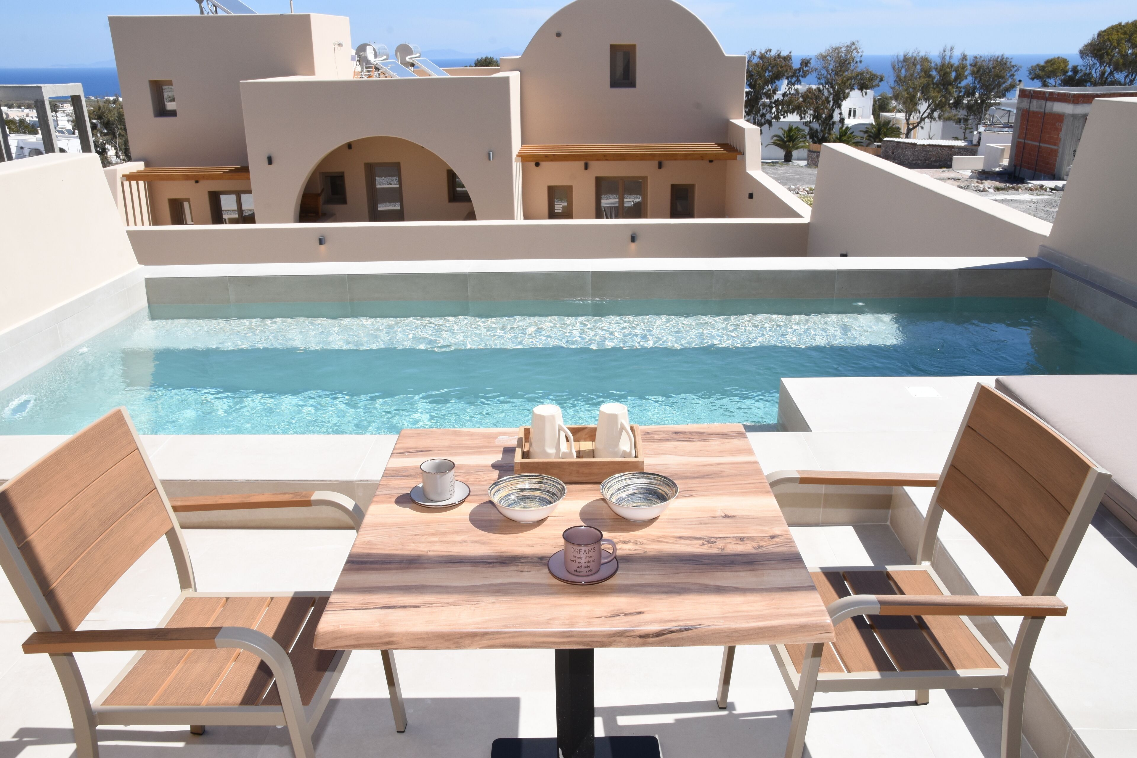 Una mesa junto a la piscina con sillas, un banco de madera, y un juego de cuencos y tazas.