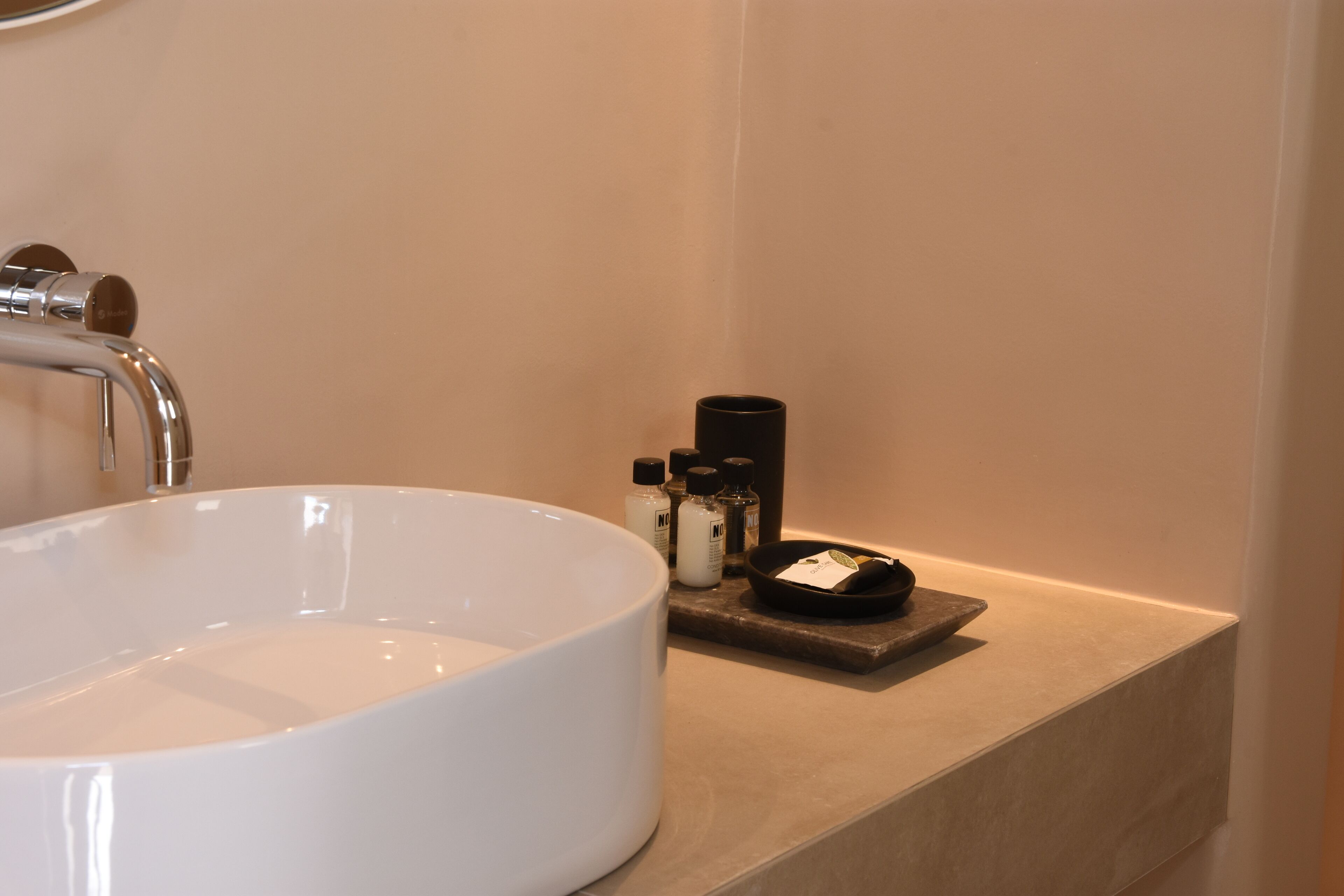 Een badkamer met een groot wit wastafel, een kraan en een plank met toiletartikelen.