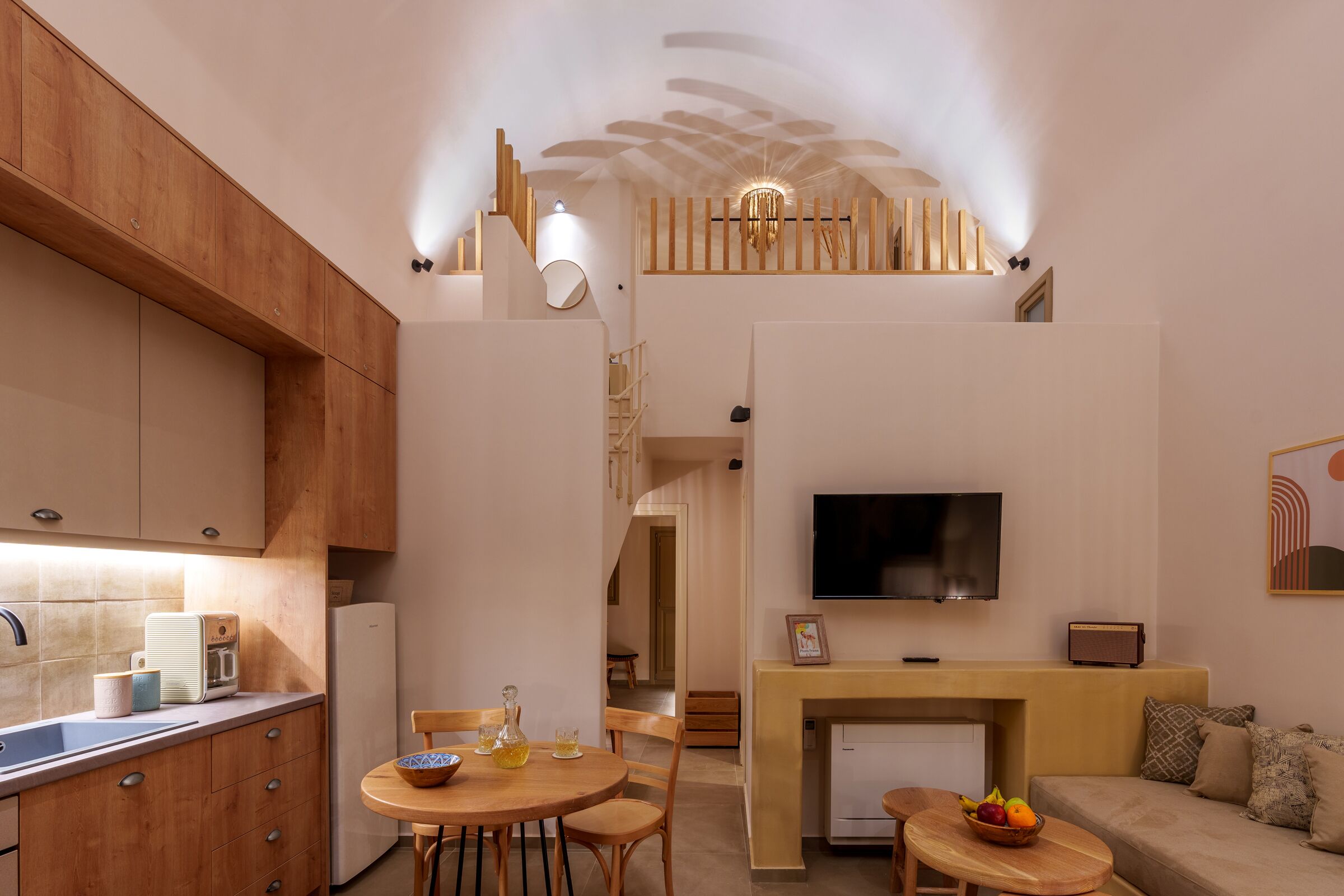 A modern kitchen with wooden cabinets, a dining area with a round table and chairs, a built-in TV, and a fireplace.