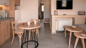 A modern living room with a fireplace, a television mounted on the wall, and a dining area with wooden furniture. - Living Moments (Santorini)
