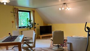 En stue med trægulv, fjernsyn, sofa, lænestol og et bord.