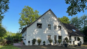 Et hvidt hus med to etager, skråtag, mange vinduer og en belagt indkørsel.