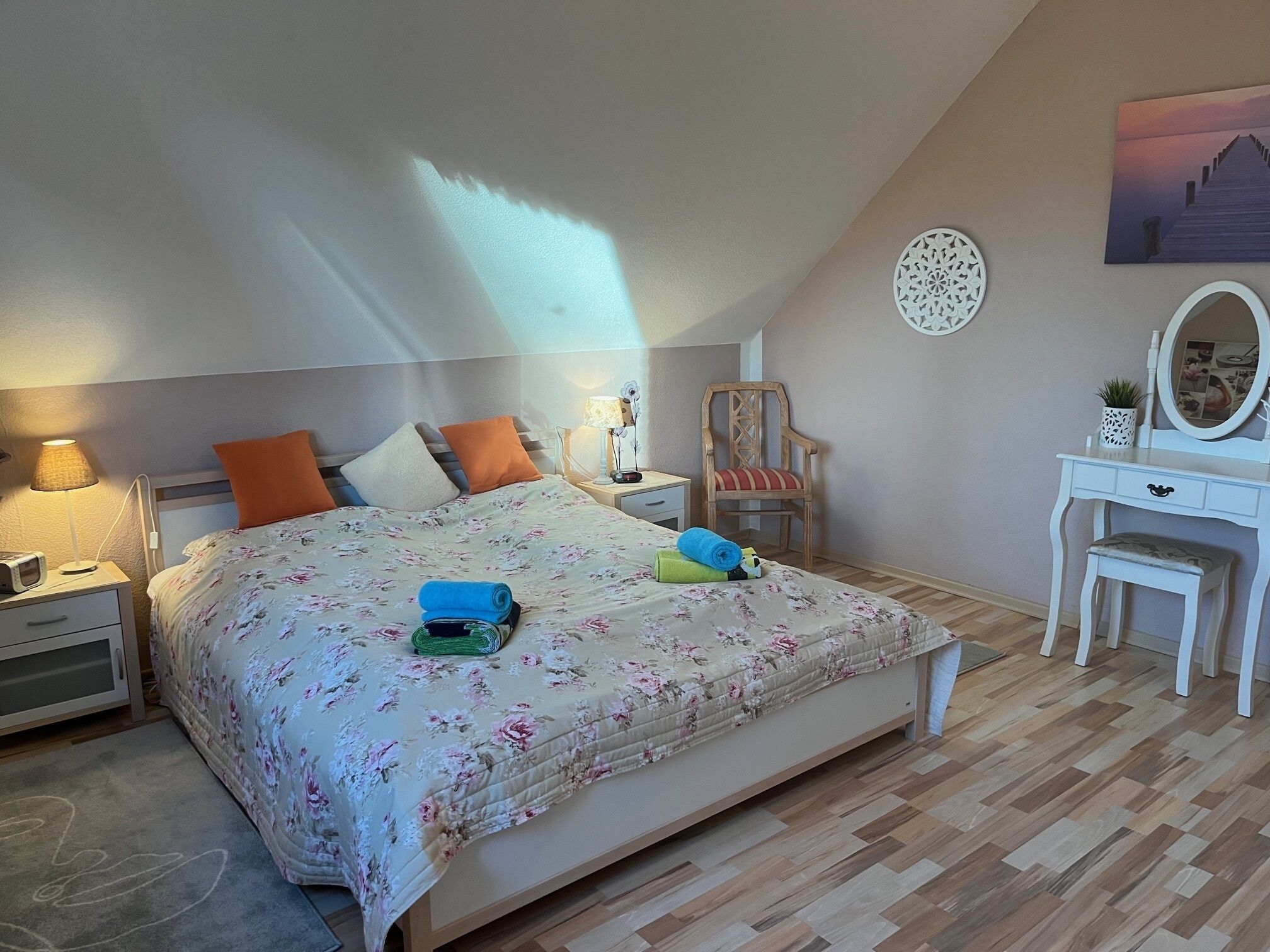 Un dormitori amb un llit, sivelles, una cadira, un prestatge i un quadre a la paret.