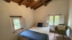 A bedroom with a bed, two windows, a chair, and a wooden ceiling. - Charming house in old stone wall village (Fibbiano)