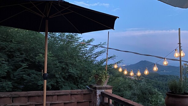 An outdoor patio with a wooden table and chairs, surrounded by a brick wall and potted plants. - Charming house in old stone wall village (Fibbiano)